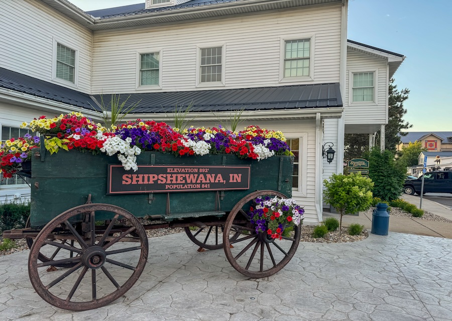 Image of buggy filled with colorful flowers and Shipshewana plaque with population sign - Guide to Shipshewana