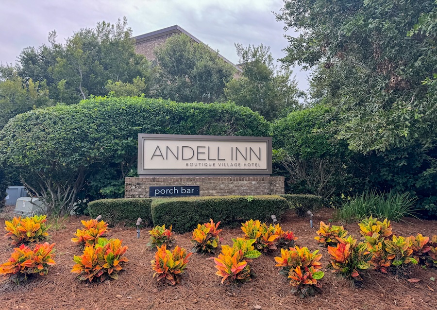 Image of entrance sign to the Andell Inn surrounded by green hedges and beautiful flowers. 